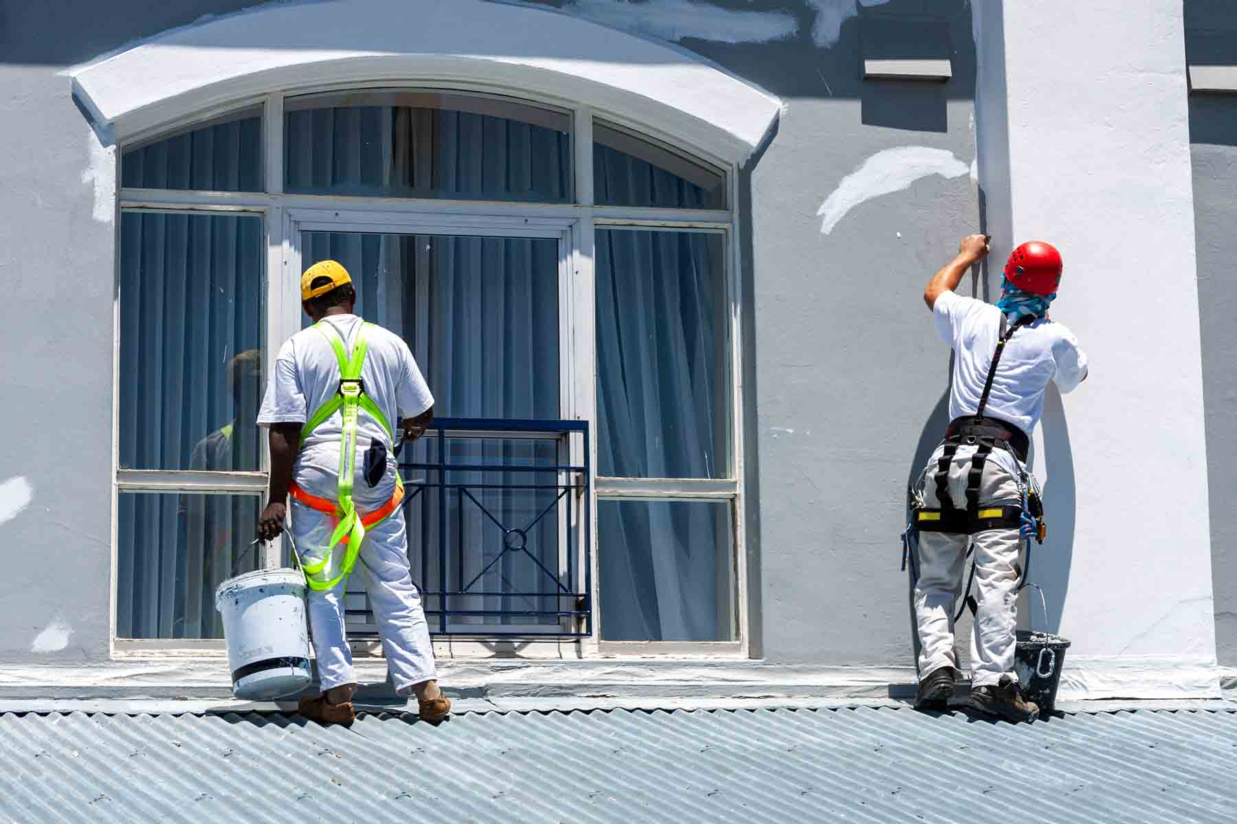 Two painters in safety harnesses repainting a commercial building exterior