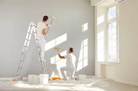 Two painters rolling white paint on office building interior walls
